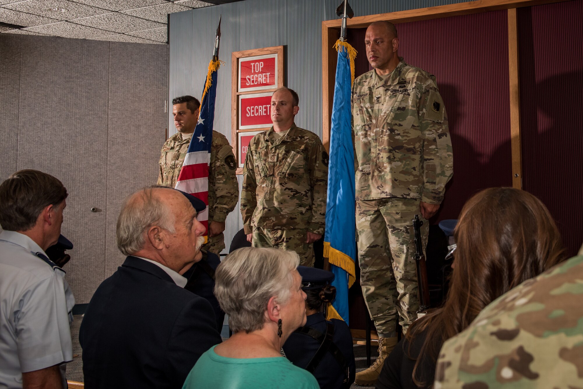 Master Sgt. Adam Hinsperger (left), 285th Special Operations Intelligence Squadron (SOIS) intelligence analyst, Master Sgt. Casey Ray (middle), 285th SOIS intelligence analyst, and Major General Michael Thompson, Adjutant General for Oklahoma, stand at attention as the color guard exits after the playing of the National Anthem during an award ceremony Aug. 4, 2018, at Will Rogers Air National Guard Base, Oklahoma City.