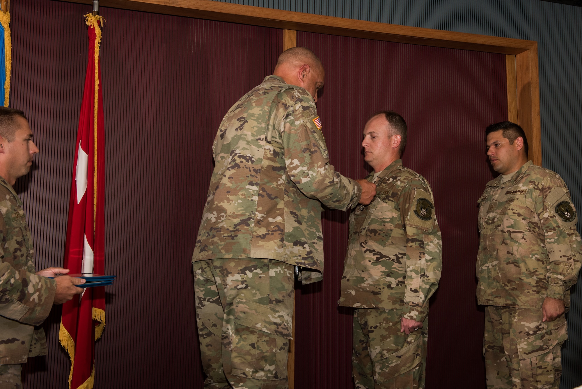 Major General Michael Thompson, Adjutant General for Oklahoma, pins a medal on Master Sgt. Casey Ray, 285th Special Operations Intelligence Squadron (SOIS) intelligence analyst, as Master Sgt. Adam Hinsperger, 285th SOIS intelligence analyst, waits to receive his award during an award ceremony Aug. 4, 2018, at Will Rogers Air National Guard Base, Oklahoma City.