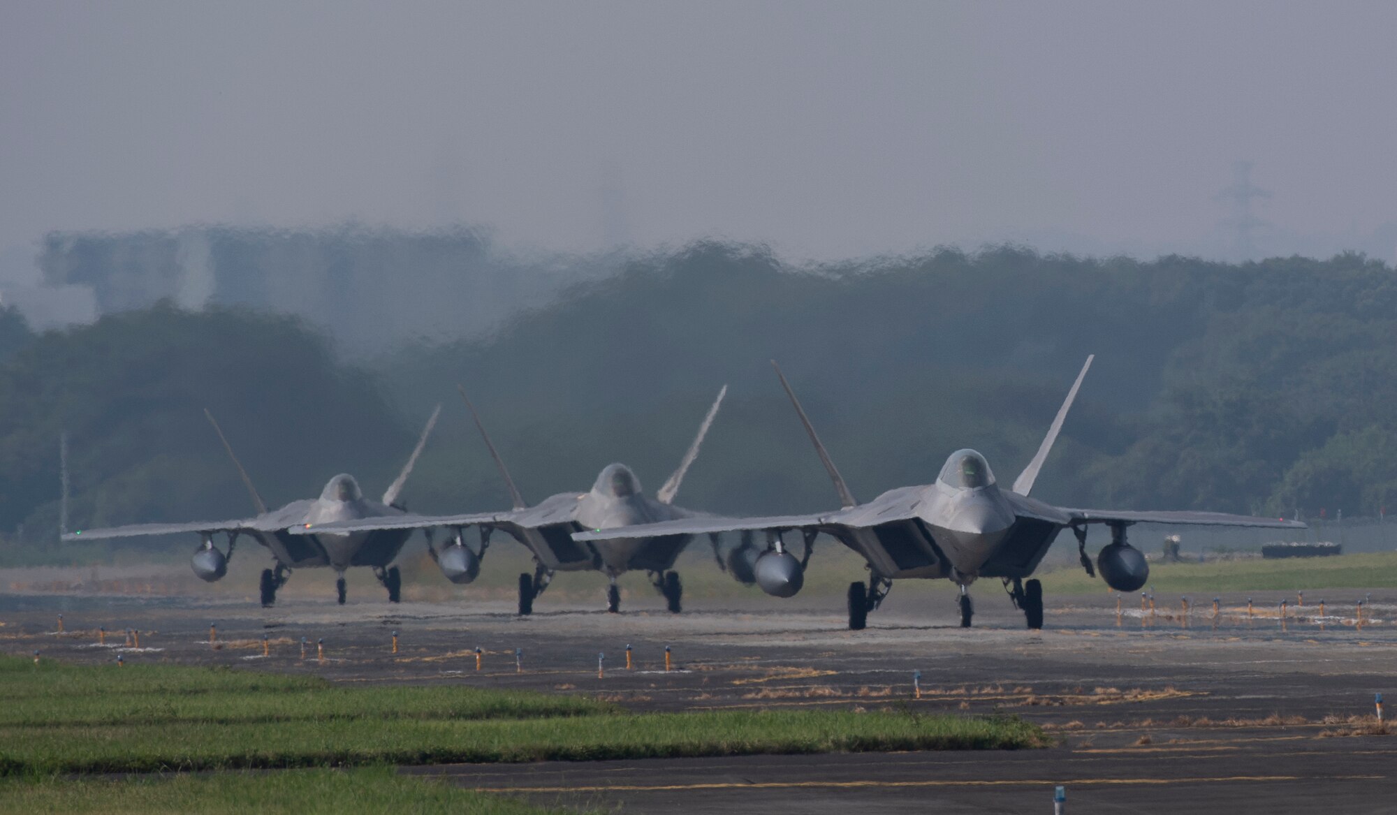 Three F-22 Raptors from Joint Base Elmendorf-Richardson, Alaska taxi down the flightline at Yokota Air Base