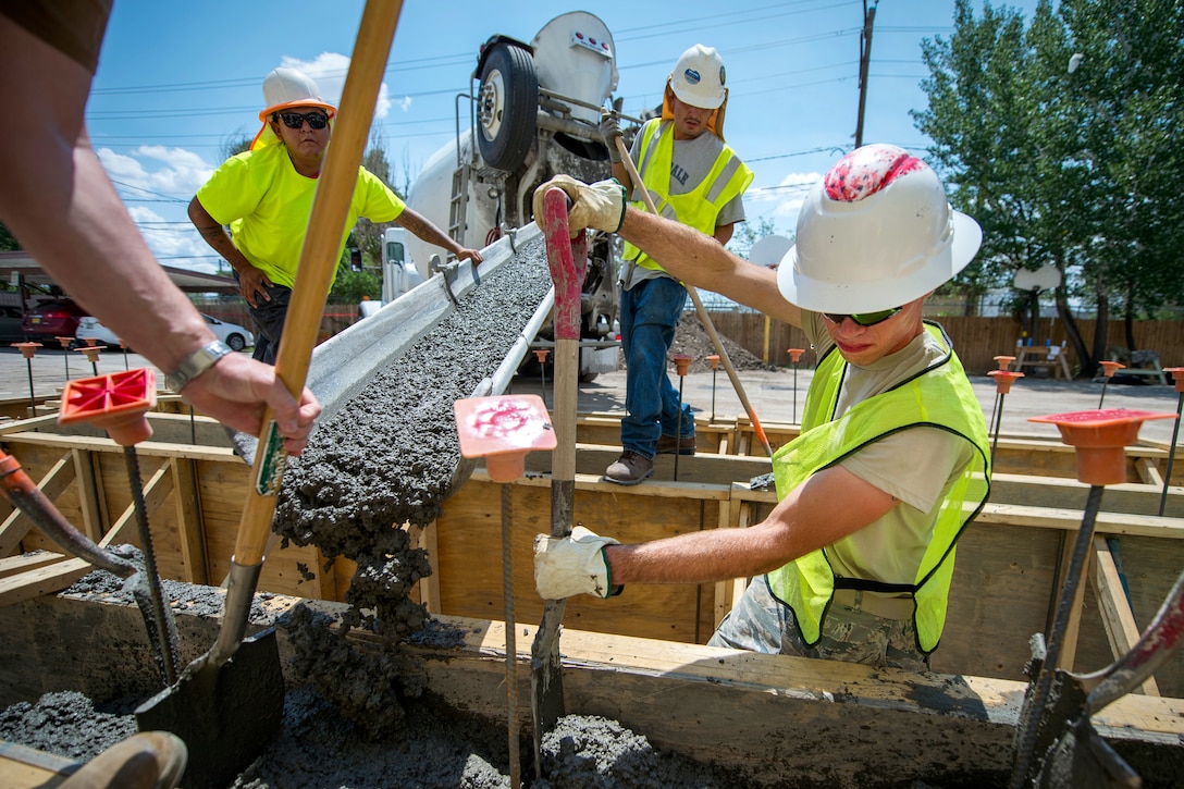 An airman spreads concrete in a form on the ground.