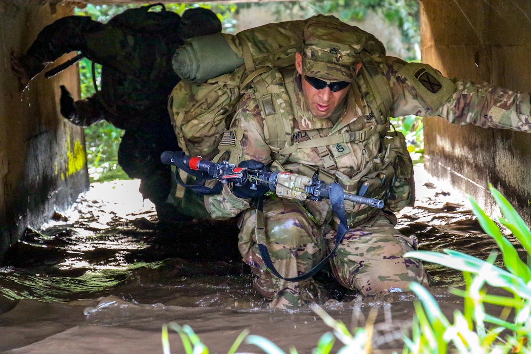 A soldier wades through the water in a tunnel.