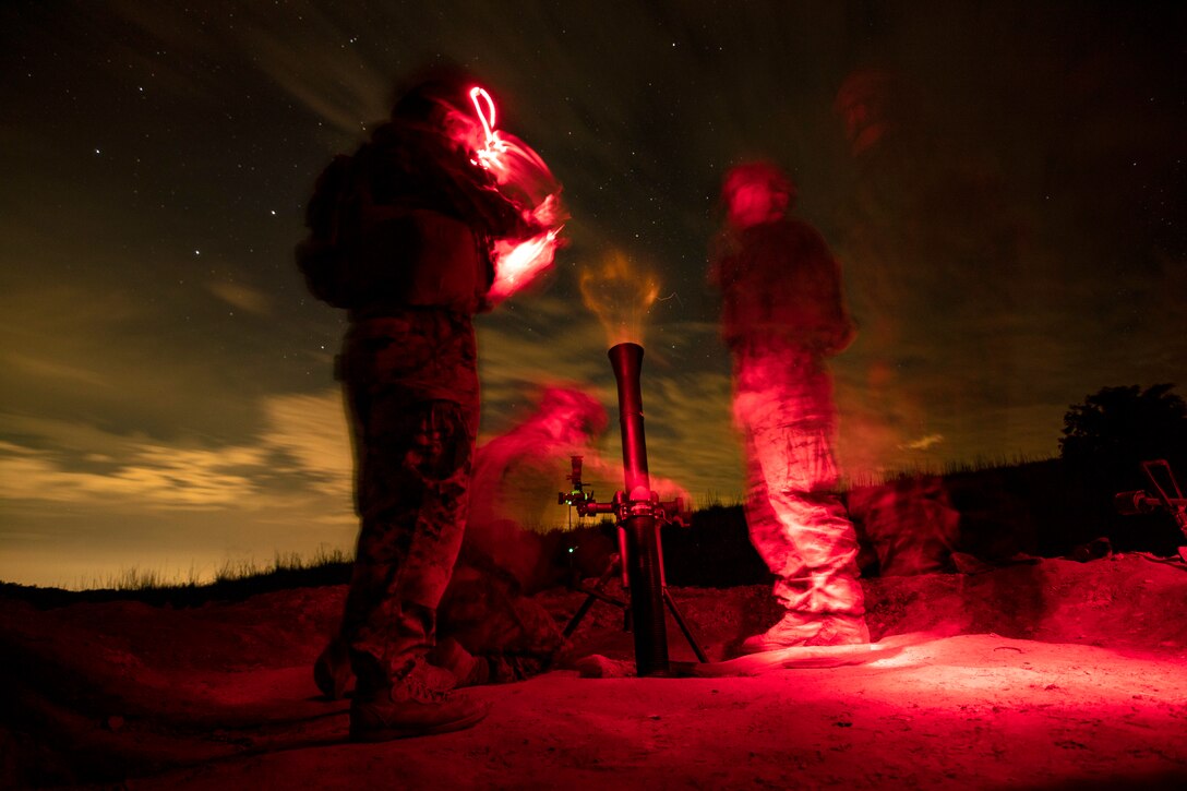 Marines fire a mortar at night.