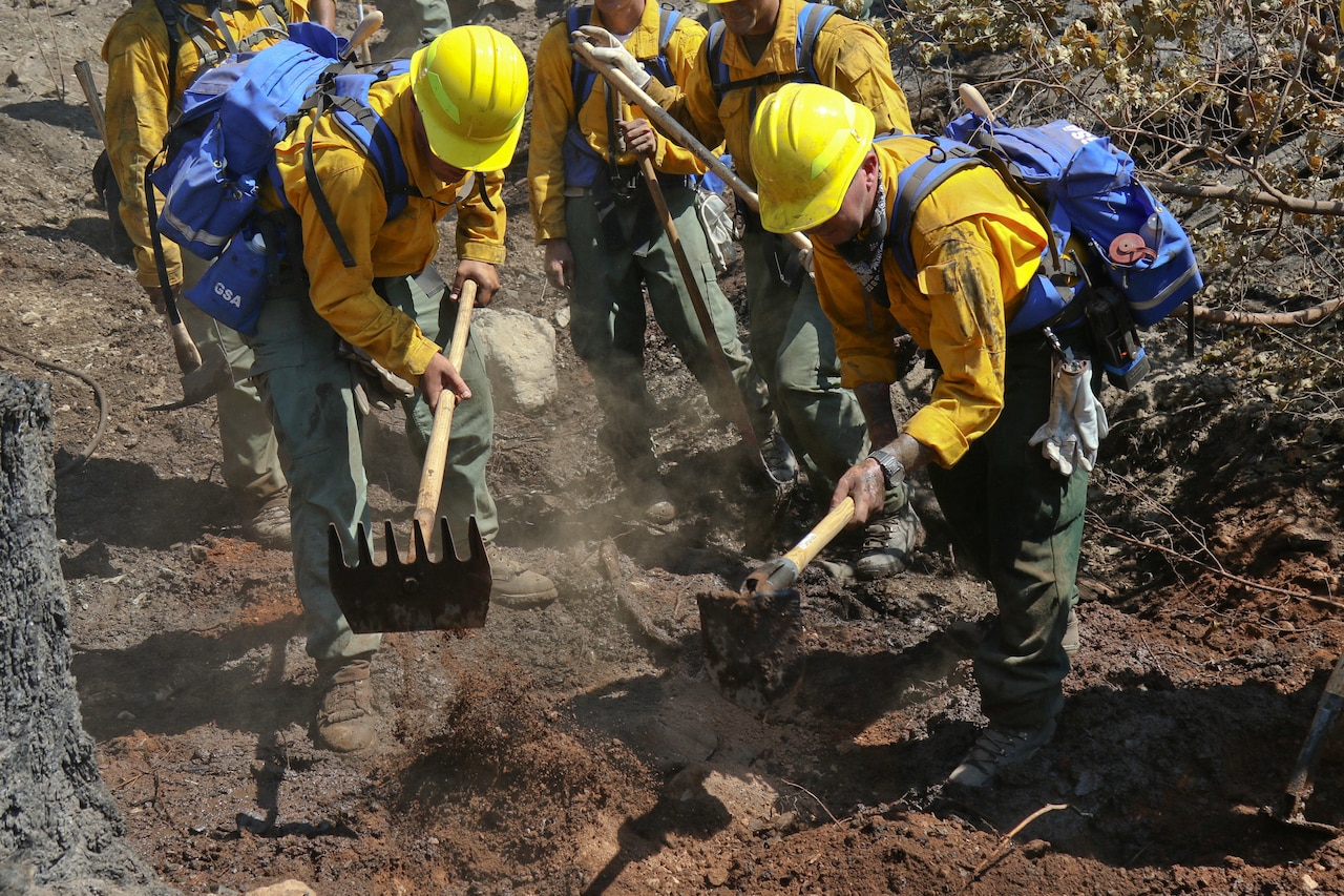 Army National Guardsmen and firefighters dig a trench to stop a fire from spreading.