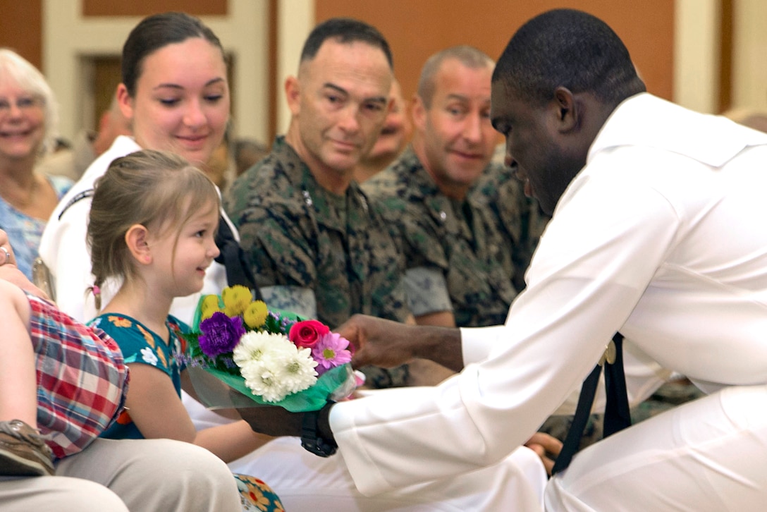 A sailor gives flowers to a sitting child.