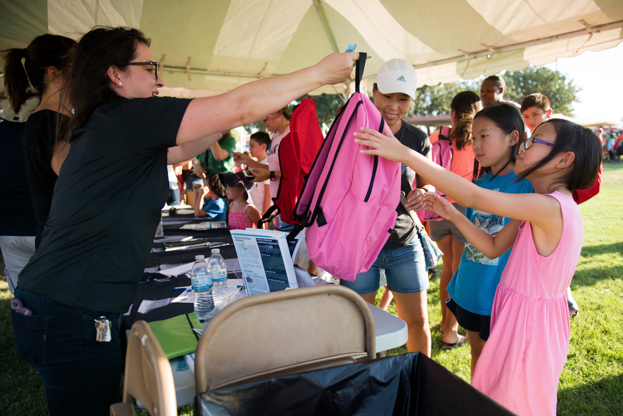 A volunteer hands a backpack to a girl at the Back-To-School Bash July 25, 2018, at Luke Air Force Base, Ariz. Freebies at the Bash included notebooks, folders, binders, markers, crayons, and many other items. (U.S. Air Force photo by Senior Airman Ridge Shan)