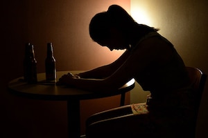 A woman sits in the dark leaning forward on a table.