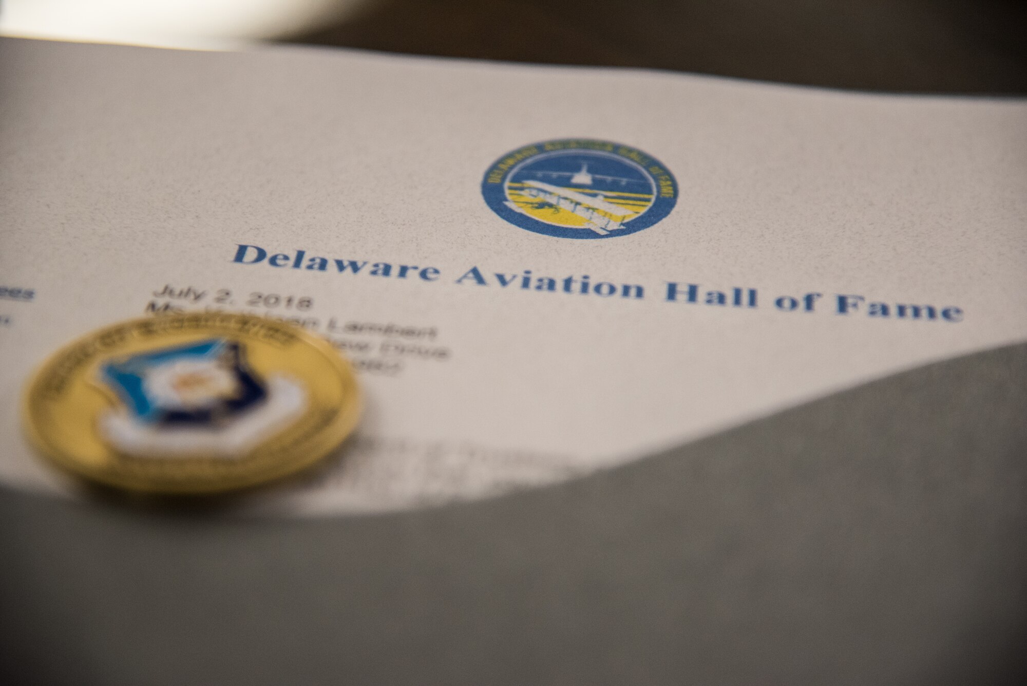 A 512th Airlift Wing coin and an official Delaware Aviation Hall of Fame inductee letter are photographed at Dover Air Force Base, Del., Aug. 3, 2018. The Delaware Aviation Hall of Fame was established to honor aviation greats and promote recognition to flyers in Delaware and flyers who defended the United States. (U.S. Air Force photo by Staff Sgt. Damien Taylor)