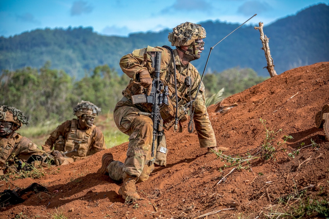 A soldier looks over a mound of dirt.