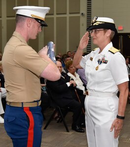 Rear Adm. Rebecca McCormick-Boyle (right), commander, Navy Medicine Education, Training and Logistics Command, completes a flag-passing ceremony during her retirement ceremony, presenting the ensign to her son, Marine Capt. Toby Boyle. The flag presented to Boyle draped the coffin of Cmdr. Carey T. Boyle, McCormick-Boyle’s deceased husband and father of Capt. Boyle.