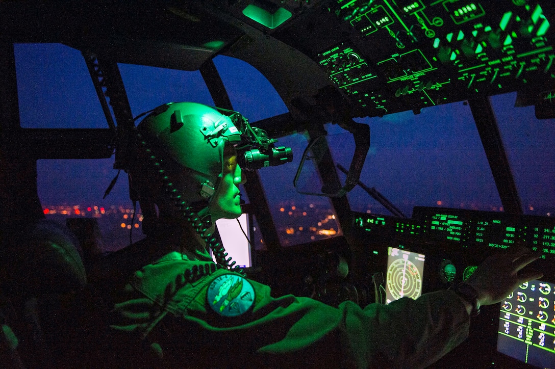 A pilot wears night vision goggles while sitting in a cockpit.