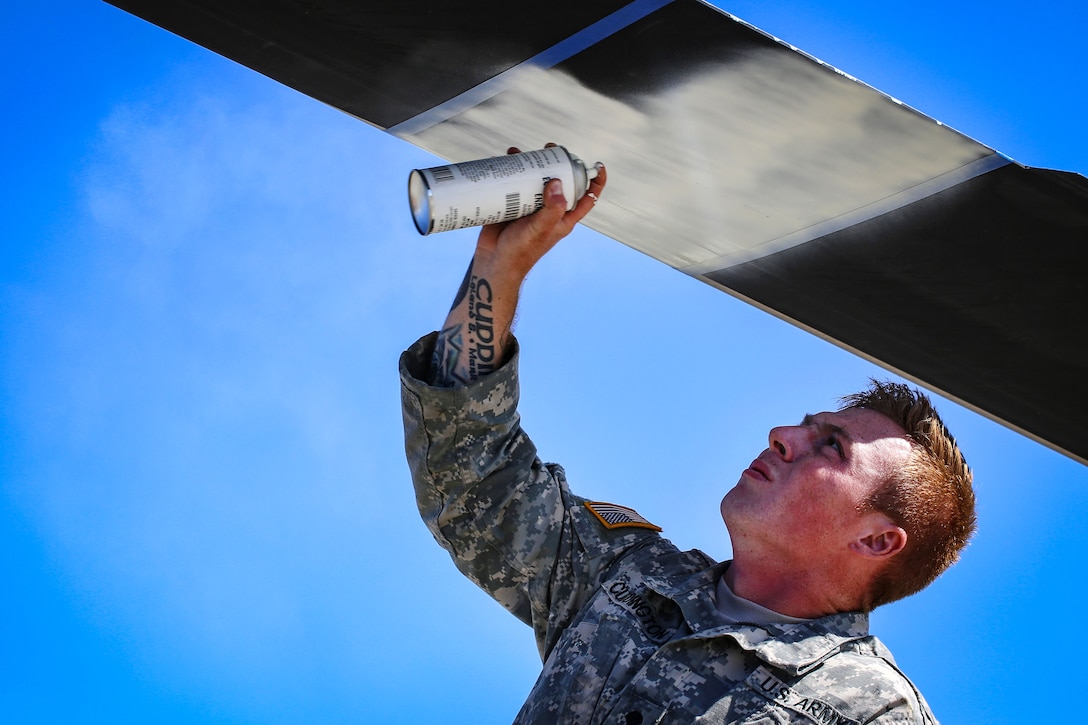 A soldier sprays white paint on a section of the rotor blades of a helicopter.