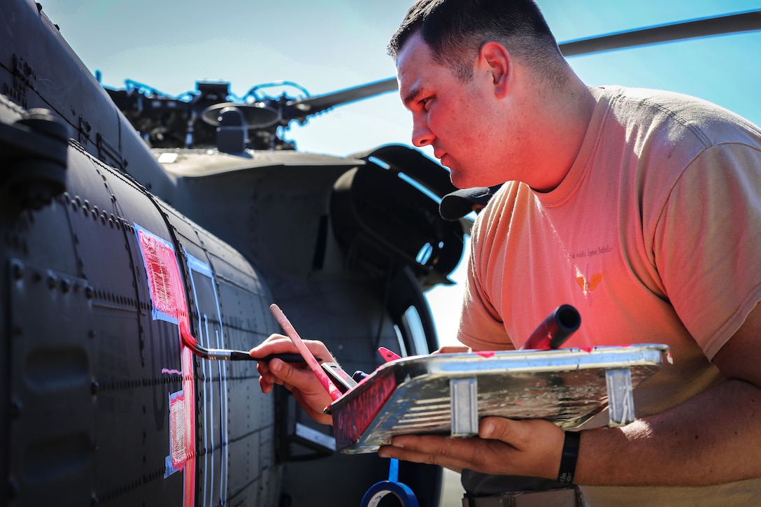 A soldier paints numbers and stripes on the side of a helicopter.