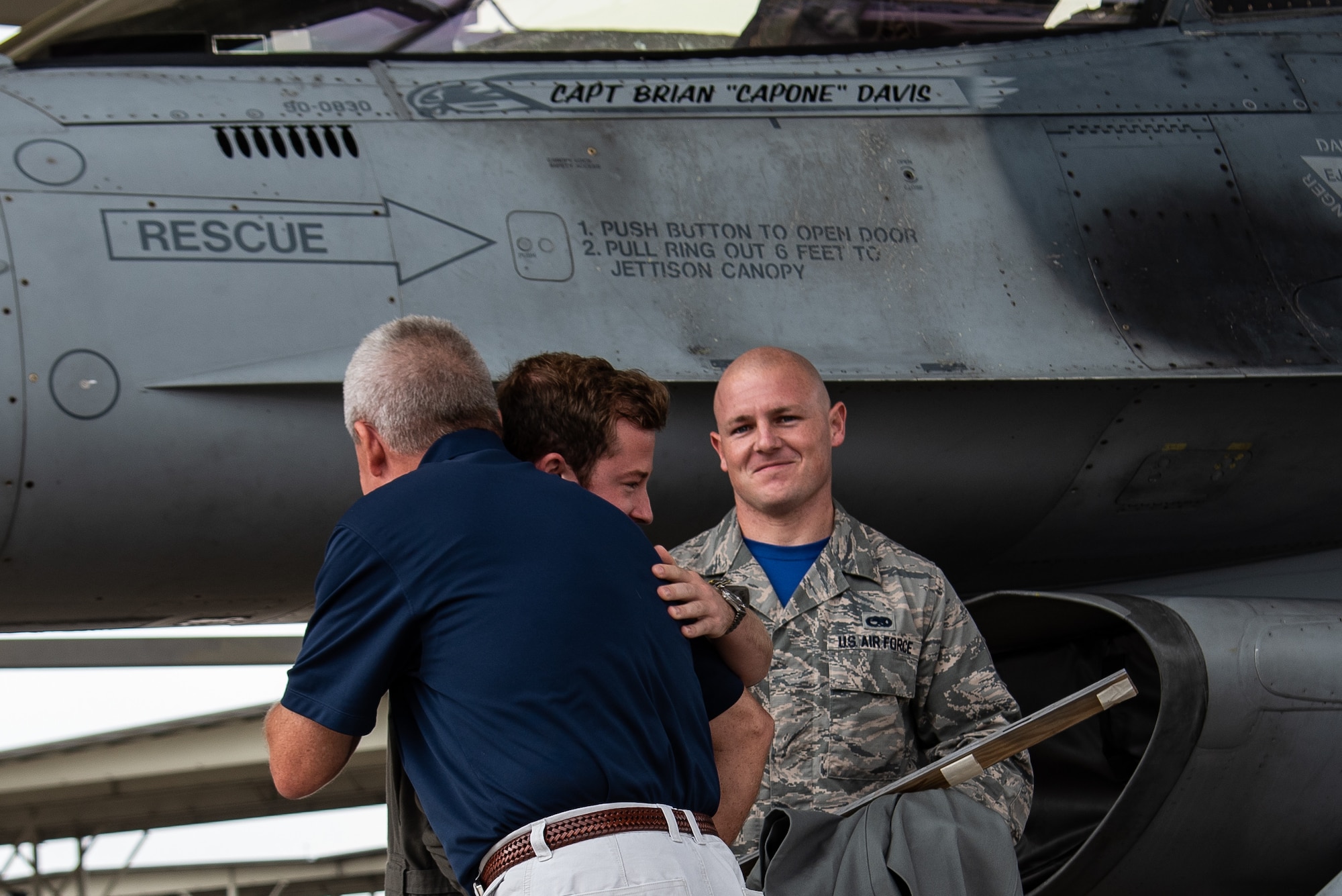 Retired U.S. Air Force Col. Rick Davis, former F-16 pilot, hugs his son, Capt. Brian Davis, 55th Fighter Squadron (FS) F-16 pilot, as Staff Sgt. Tyler Roecker, 20th Aircraft Maintenance Squadron dedicated crew chief, watches after a ceremony at Shaw Air Force Base, S.C., Aug. 3, 2018.