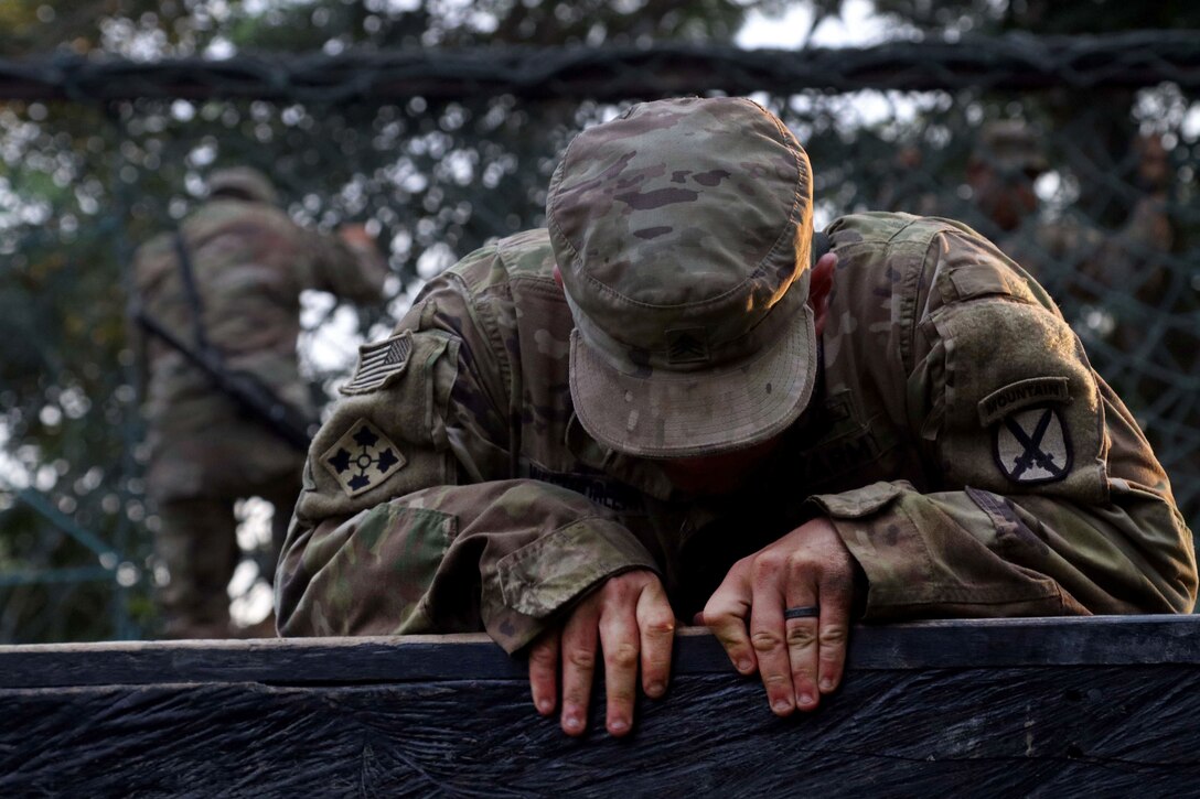 A soldier climbs over a six foot wall on the obstacle course.