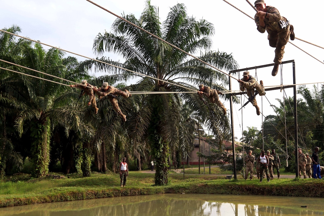 U.S. soldiers negotiate the rope bridge over a pond.