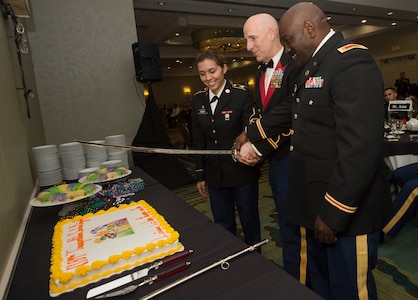 From left to right, U.S. Army Pvt. Christina Chavis, 82nd Distribution Deployment Support Battalion, Col. Daniel Keller, 1189th Transportation Surface Battalion outgoing commander, and Chief Warrant Officer Curtis Wilson, 1189th TSB mobility warrant officer, cut a cake during the 1189th TSB Mardi Gras Masquerade Ball at the Crowne Plaza Charleston Airport Hotel Aug. 4, 2018, in North Charleston, S.C. The youngest and oldest Soldier in attendance were selected to cut the cake with Keller.