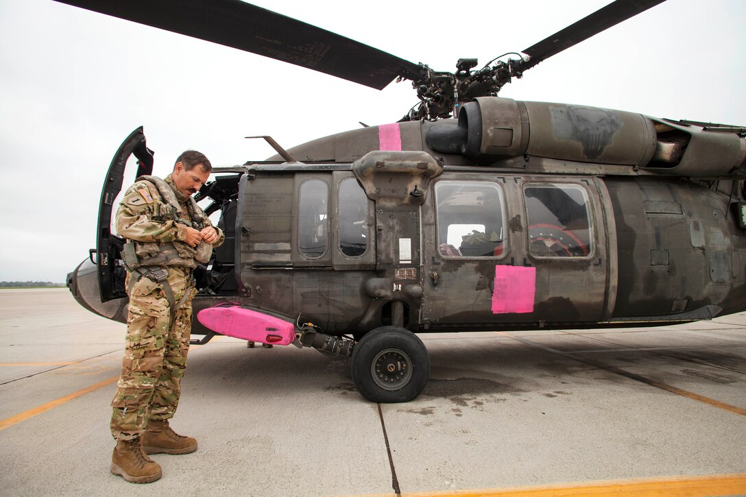 A pilot prepares his gear before flying a UH-60L Black Hawk helicopter.