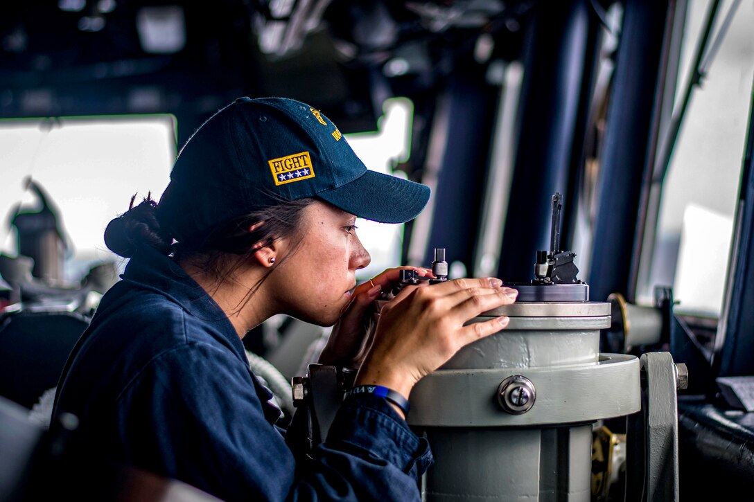 A sailor leans over equipment.