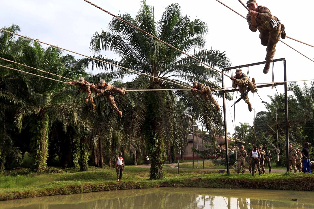 U.S. soldiers negotiate the rope bridge over a pond.
