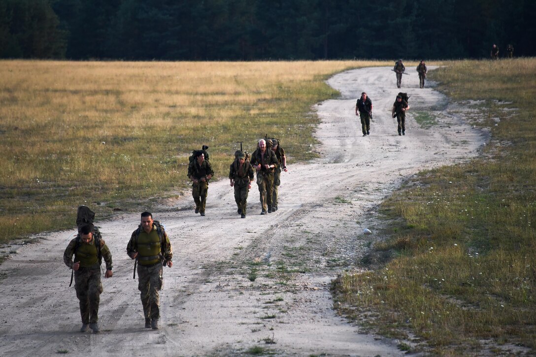 U.S. soldiers and NATO sniper teams participate in the ruck march along a dirt road.