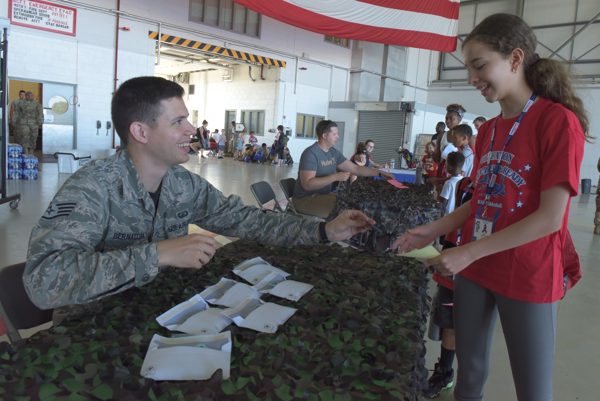 U.S. Air Force Staff Sgt. Dimas Bernacchia, 100th Comptroller Squadron financial management technician, in processes a girl during the ‘kids deployment line’ at RAF Mildenhall, England, Aug. 3, 2018. The “kids deployment line,” or Operation Together and Ready, had 150 kids in attendance to learn about deployed life. (U.S. Air Force photo by Senior Airman Kelly O’Connor)
