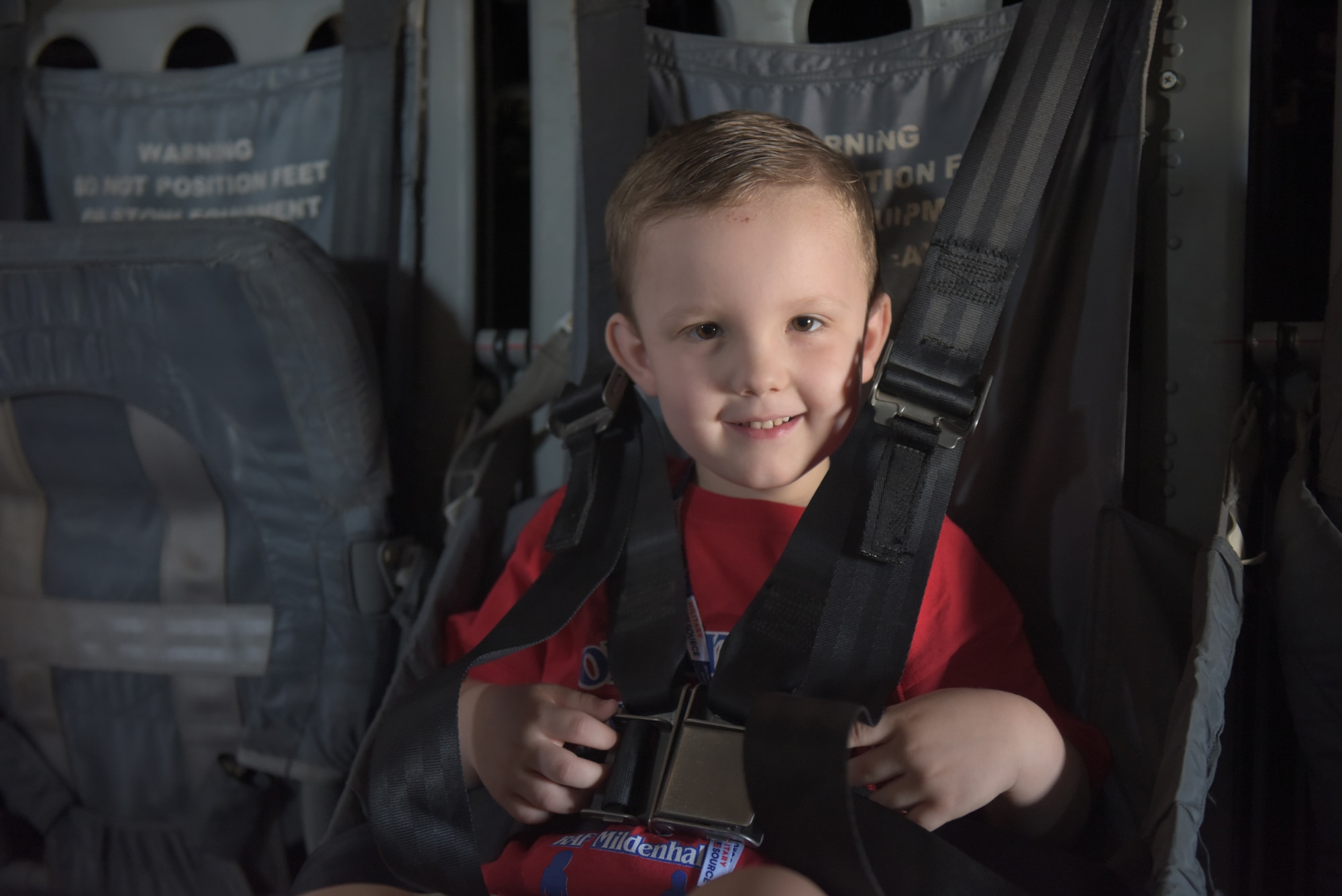 A boy is buckled into the seat of a CV-22 Osprey at RAF Mildenhall, England, Aug. 3, 2018. An MC-130J Commando and a KC-135 Stratotanker were also on display during the “kids deployment line.” (U.S. Air Force photo by Senior Airman Kelly O’Connor)