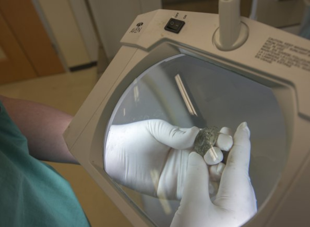 A lab worker holds an item under a magnifying panel.