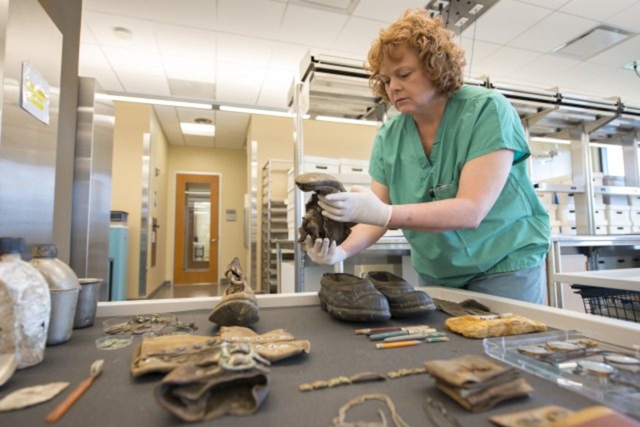 A lab worker examines personal effects that may have belonged to a fallen service member.