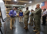 Marc Marquez, Bin Division Chief, is explaining the production board to the DLA Director as DLA Distribution Commanding Officer Navy Rear Adm. Kevin Jones and DLA Distribution San Joaquin Commander Marine Col. Andre Harrell listen.