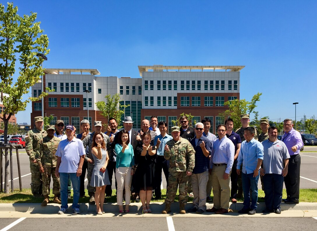 Group photo, facing viewer; red/white brick building in background under blue sky