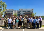 Group photo, facing viewer; red/white brick building in background under blue sky