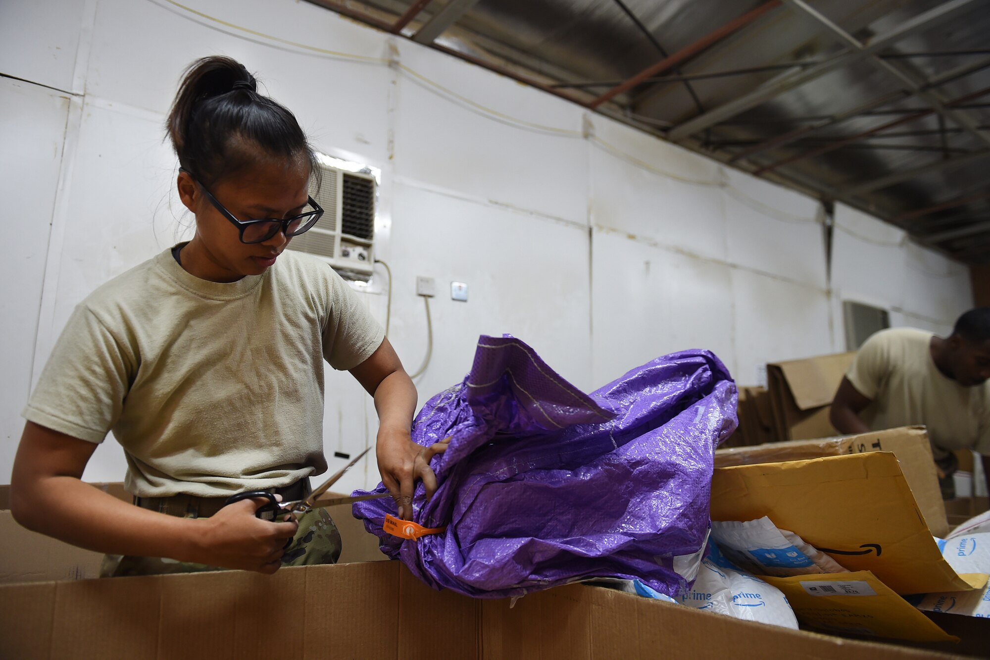 A female Airman cuts a bag of mail open with scissors