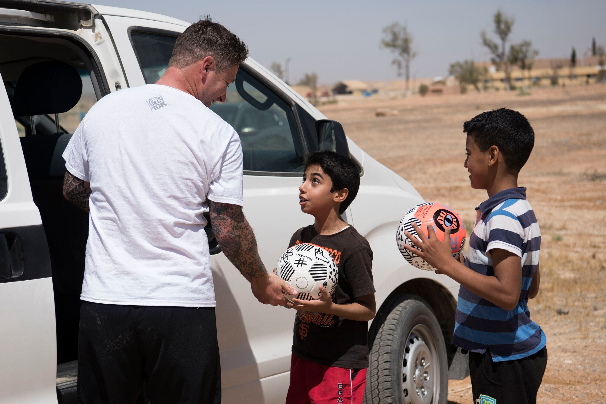 Senior Airman Timothy Jones, 332nd Expeditionary Medical Group medical logistician, hands out donated soccer balls to local kids at an undisclosed location in Southwest Asia May 26, 2018.