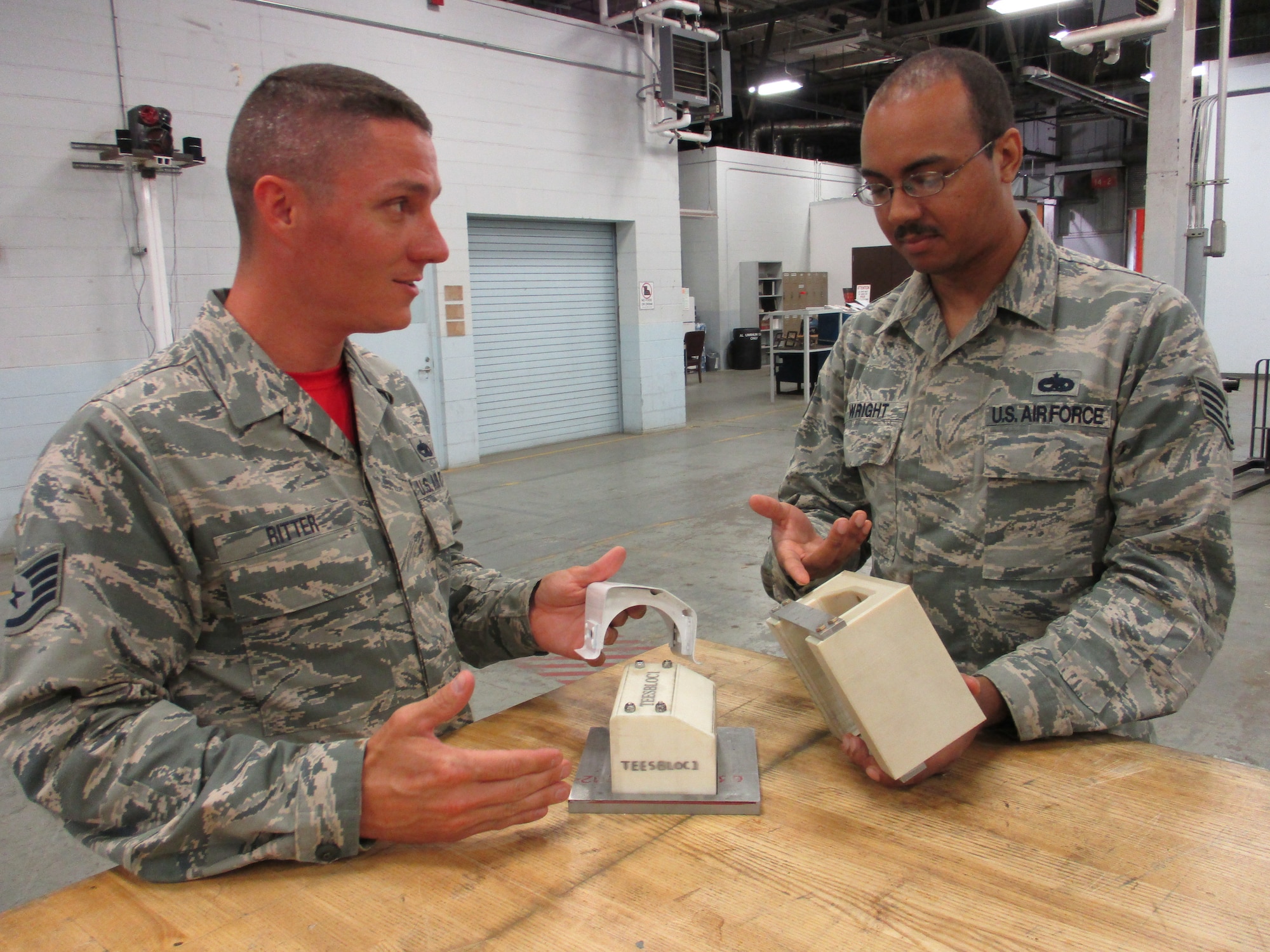 Staff Sgt. Christopher Ritter, 513th Maintenance Squadron Section Chief, and Staff Sgt. Michael Wright, 552nd Maintenance Squadron Aircraft Metals Technology, explain how 3-D printed parts can be so dense as to be used in hydraulic presses to bend metal into necessary shapes without any damage. (U.S. Air Force photo by Master Sgt. Andrew Stephens)