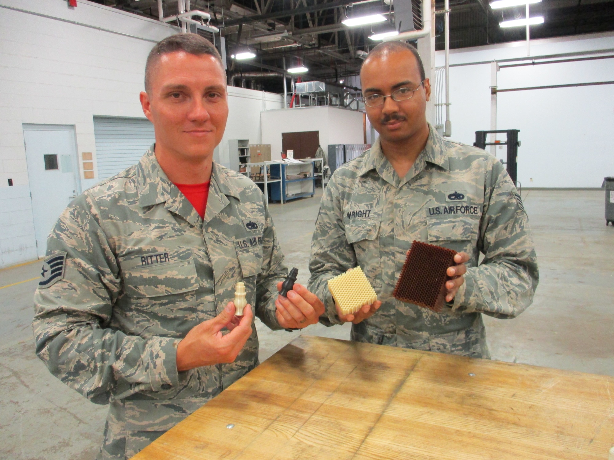 Staff Sgt. Christopher Ritter, 513th Maintenance Squadron Section Chief, and Staff Sgt. Michael Wright, 552nd Maintenance Squadron Aircraft Metals Technology, show the difference between 3-D printed parts and manufactured parts.  Whether printing up something as simple as a plastic seat handle or as complex as a replacement for phenolic resin honeycomb, 3-D printing saves Tinker AFB's Team AWACS time and money while improving aircraft readiness. (U.S. Air Force photo by Master Sgt. Andrew Stephens)