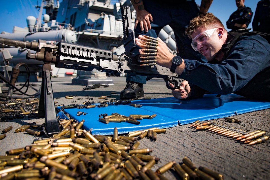 A sailor loads ammunition into an M240B machine gun.