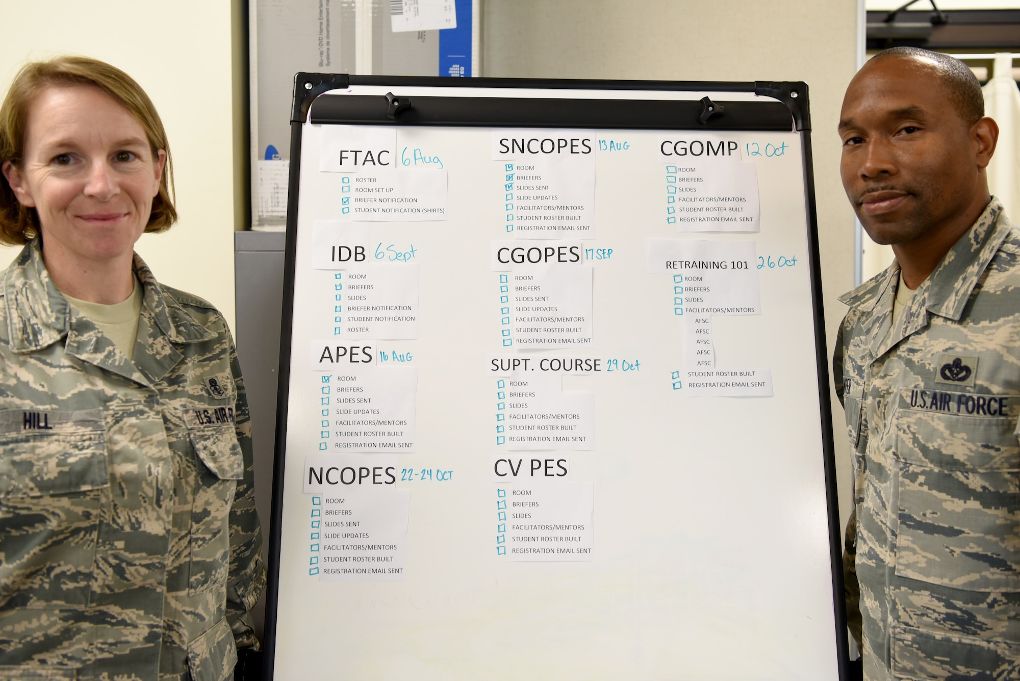 U.S. Air Force Senior Master Sgt. Brandy Hill, left, and Master Sgt. Jamell Camper, right, 20th Force Support Squadron career assistance advisors (CAA), stand next to a list of professional military education courses offered at Shaw Air Force Base, S.C., Aug. 3, 2018.