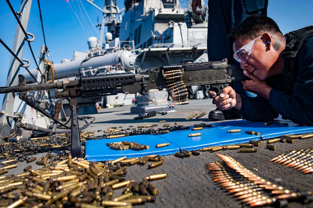 A sailor takes aim at targets while firing a M240B machine gun.