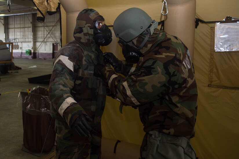 A U.S. Air Force Aircrew Flight Equipment Airman removes an aircrew member’s protective gear during Aircrew Contamination Control Area training at Joint Base Langley-Eustis, Virginia, July 12, 2018. As each aircrew member passes through the nine stations of the ACCA, a piece of their protective equipment is removed after being cleared of chemical agents. (U.S. Air Force photo by Senior Airman Derek Seifert)