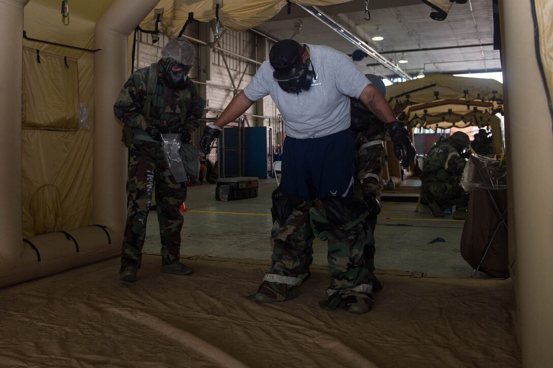 A U.S. Air Force Aircrew Flight Equipment Airman removes an aircrew member’s protective gear during an Aircrew Contamination Control Area training at Joint Base Langley-Eustis, Virginia, July 12, 2018. AFE trainers were retrained on the most current procedures of an ACCA so they can then train their Airmen. (U.S. Air Force photo by Senior Airman Derek Seifert)