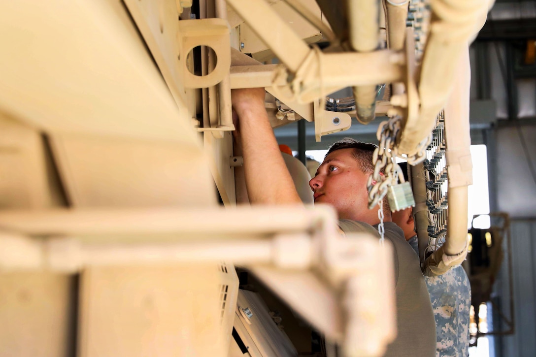 A soldier repairs a door on a tactical vehicle in a motor pool.