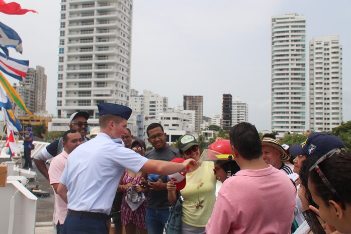 Petty Officer 2nd Class David Rice, a damage controlman aboard the Coast Guard Cutter Hamilton, helps a woman don a firefighting helmet July 24, 2018, at Sail Cartagena de Indias 2018 in Cartagena, Colombia.