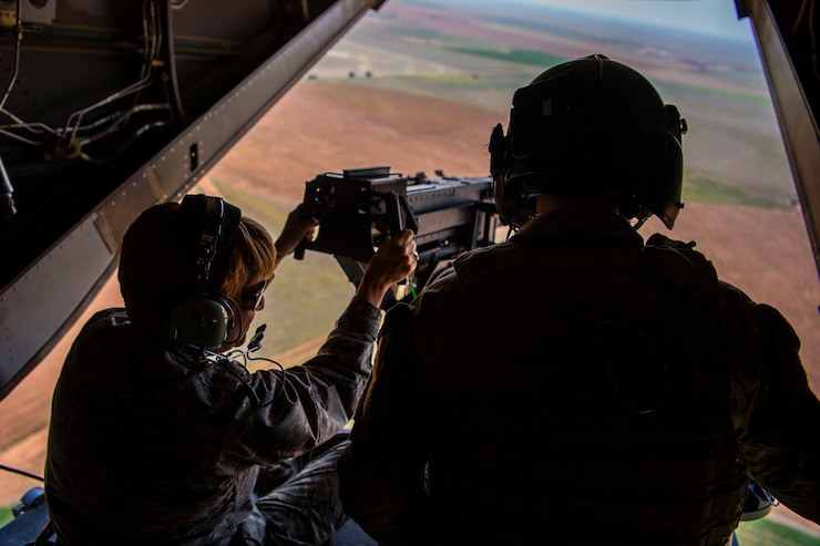 An Airman looks as another fires a machine gun from the rear of a CV-22 Osprey