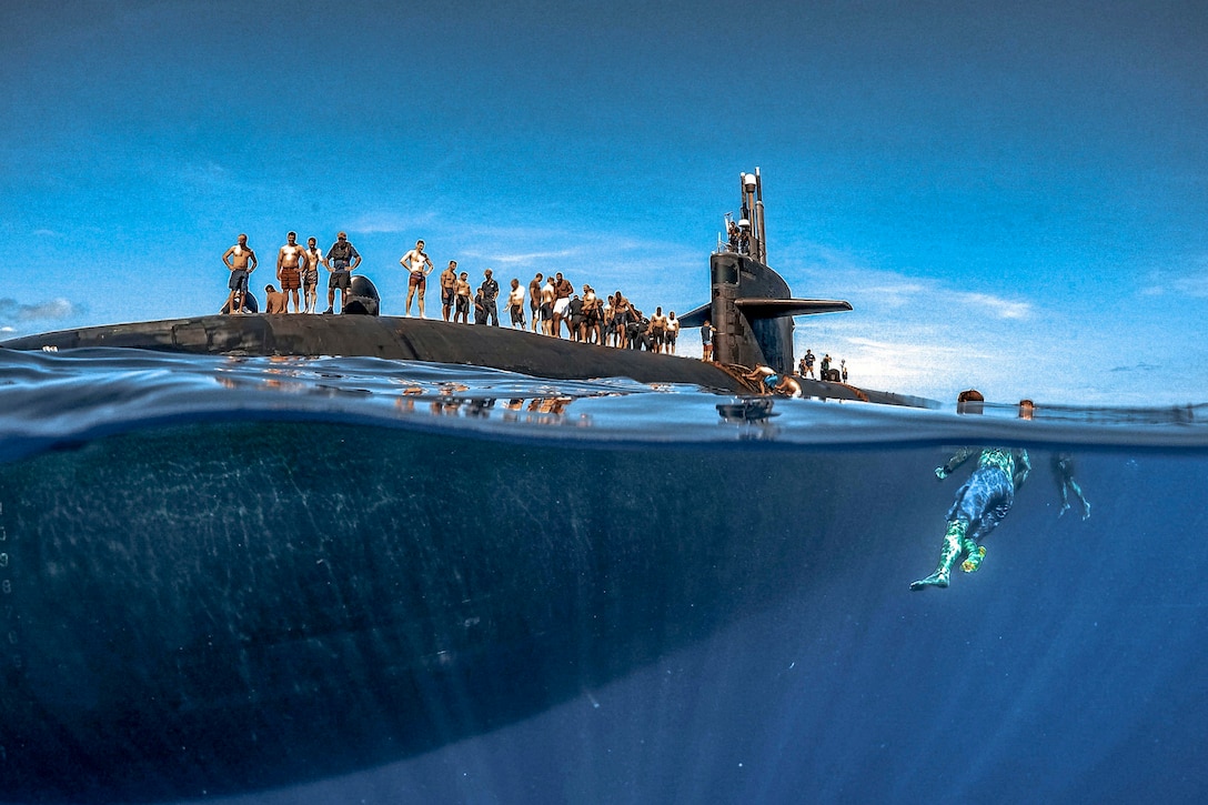 Sailors swim around a submarine.