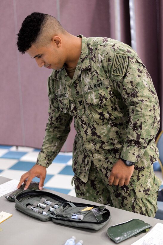 Hospital Corpsman Third Class Yunior Castano Perez, from Yokosuka Medical Center, displays the utility of the personal first aid kit issued with MOPP gear at Yokota Air Base, Japan, August 8, 2018.