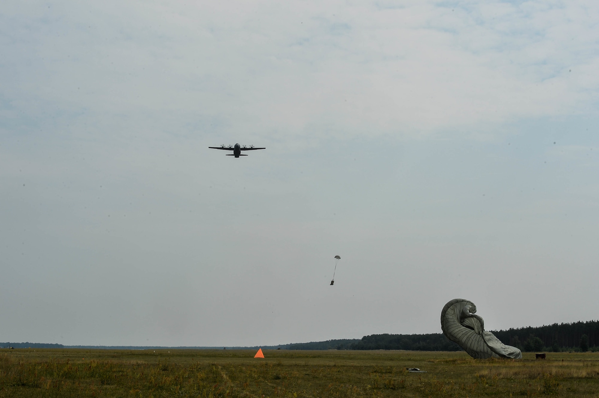 A U.S. Air Force C-130J Super Hercules flies over a drop zone as cargo delivery packages descend, over Powidz Air Base, Poland, Aug. 9, 2018. U.S. and Polish Airmen celebrated their partnership with an aerospace rodeo competition. (U.S. Air Force photo by Senior Airman Joshua Magbanua)