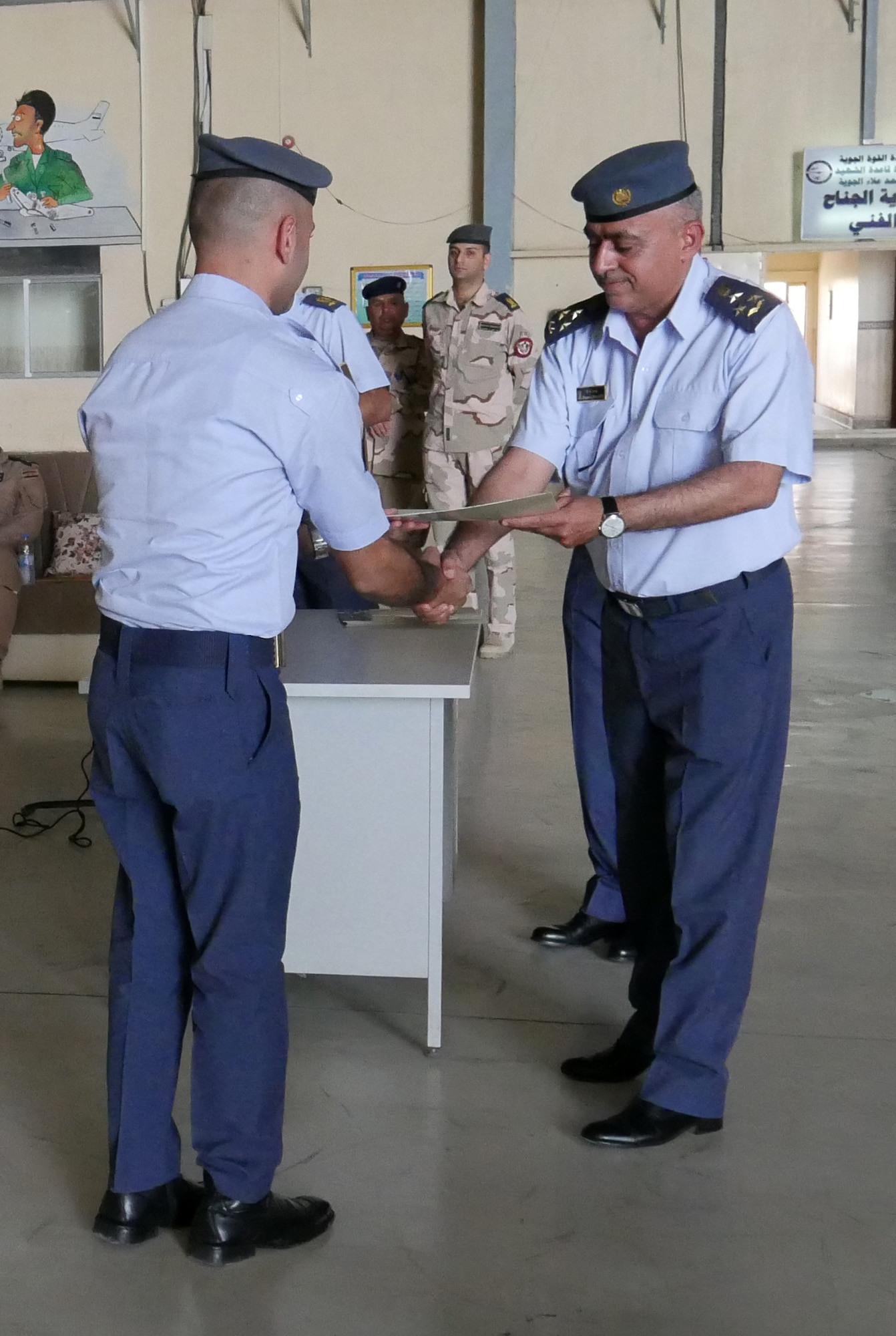 Iraqi Air Force Brig. Gen. Husni Khazaal Al Maliki, Al Muthana Technical Wing commander, hands a maintenance technician a certificate of training during an upgrade ceremony July 31, 2018. The IqAF recognized their upgraded 5- and 7-level craftsman C-130J Super Hercules maintenance technicians for the first time since late 2017. (U.S. Air Force photo by Capt. Benjamin Hughes)
