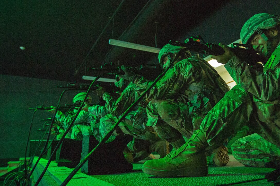 Soldiers practice marksmanship skills virtually, under green light indoors.