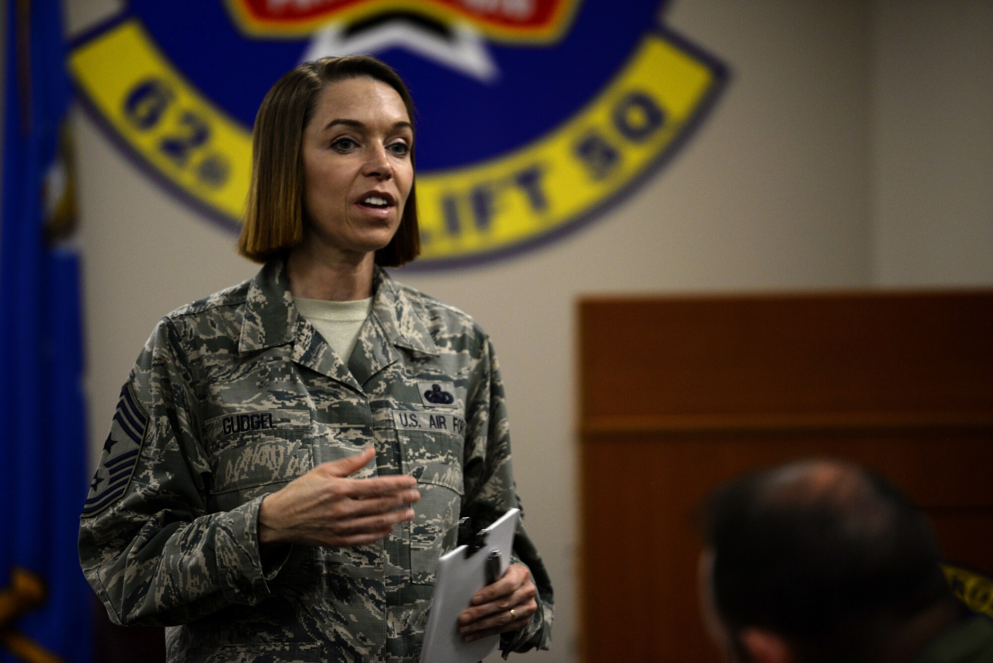 A woman in the Airman Battle Uniform holds a pad of paper while speaking to peopole in a crowd