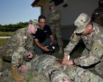 Master Sgt. Rich Jarret (right), U.S. Army Medical Department Center and School Center for Prehospital Medicine, demonstrates how to pack a gunshot wounded with gauze on the newly fielded Tactical Combat Casualty Care-Exportable mannequin that will be used train all Soldiers on basic warrior medical skills, to Command Sgt. Maj. William “Will” Rinehart, United States Army South, as Luciano Cortez, field instructor with trauma effects, controls the TC3-X and PEO-STRI clinical advisor, Lt. Col. (Dr.) Benjamin Baker looks on.